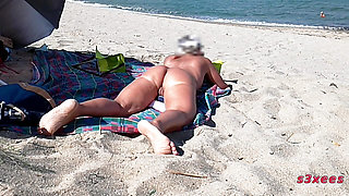 She shows her ass on the beach of Cap d'Agde and jerks off her pussy and then her boyfriend's cock with voyeurs