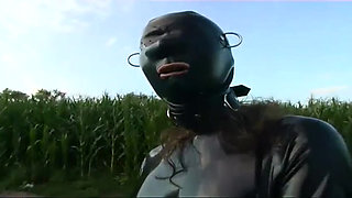 Fetish slave in latex walks and sucks a dildo on the grass